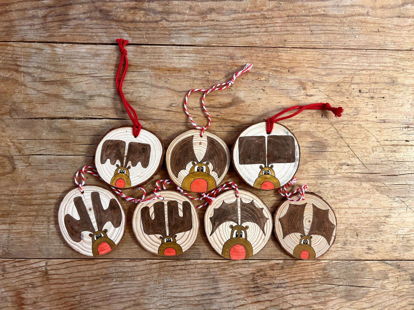 A collection of wood slice ornaments with KM Art style "Rudy" paintings. Each has a red nose and different style of antlers.