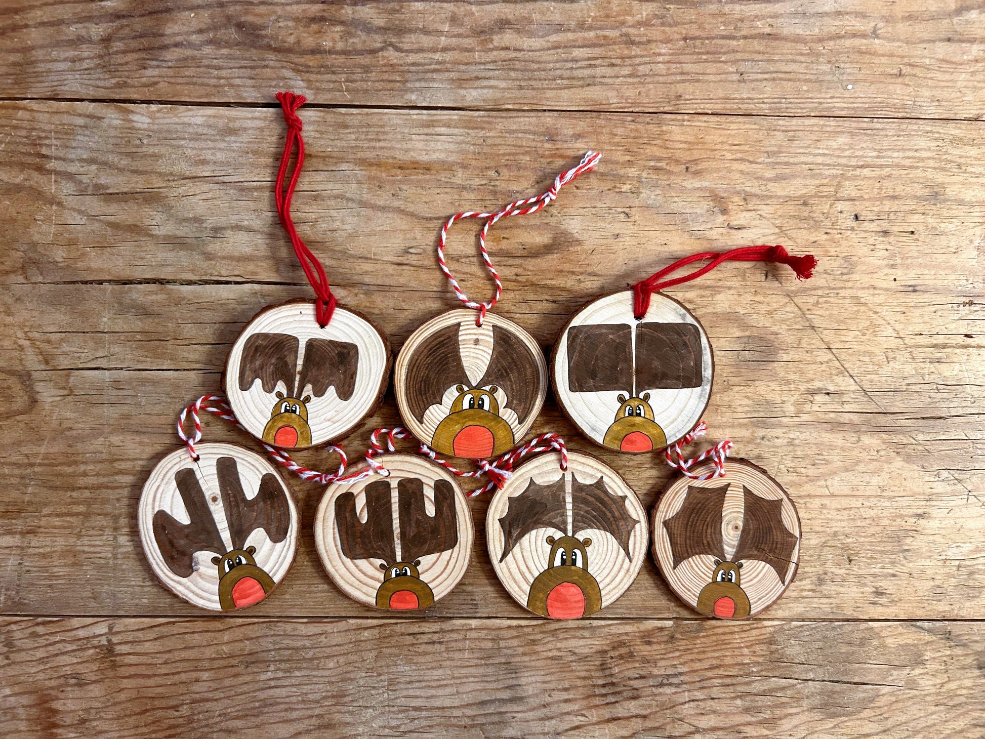 A collection of wood slice ornaments with KM Art style "Rudy" paintings. Each has a red nose and different style of antlers.