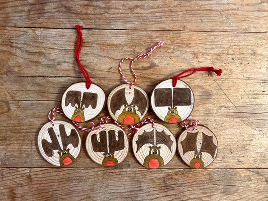 A collection of wood slice ornaments with KM Art style "Rudy" paintings. Each has a red nose and different style of antlers.