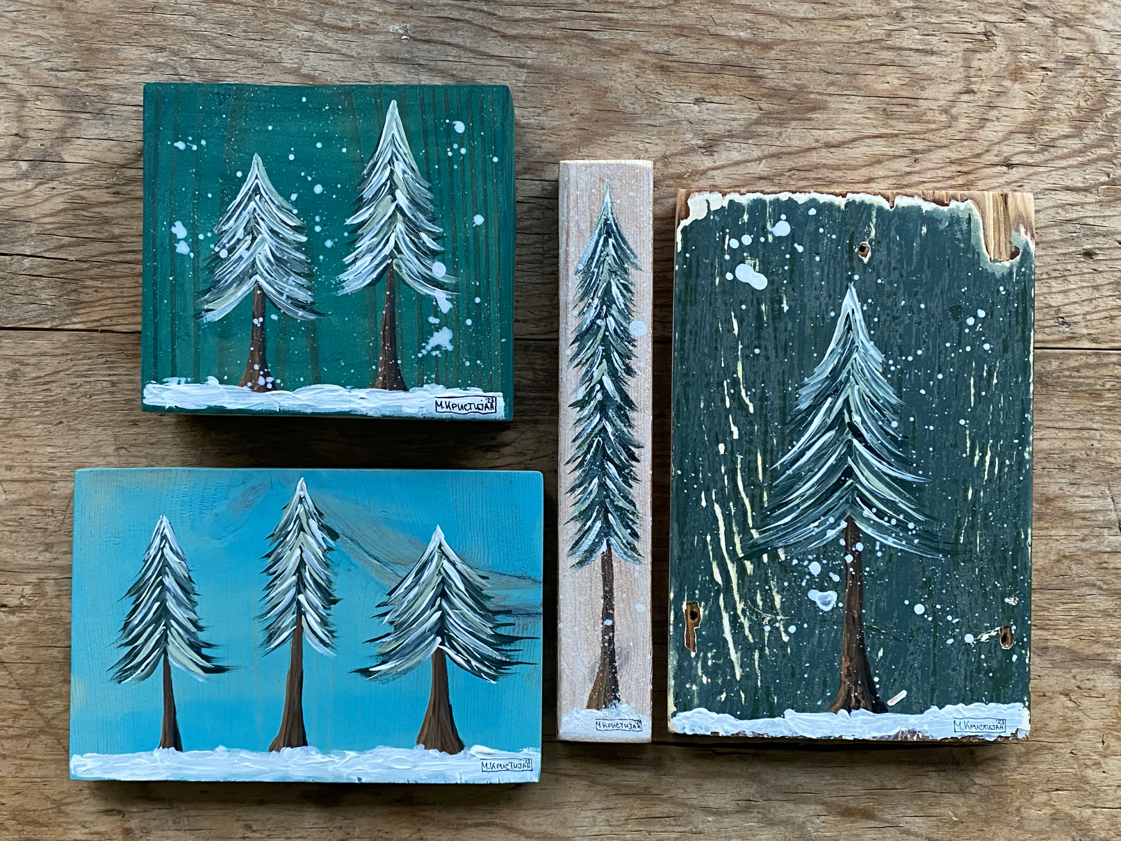 A set of three decorative acrylic paintings of winter fir trees on reclaimed wood, displayed on a wooden surface.